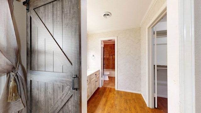 hallway with a barn door, light hardwood / wood-style flooring, and ornamental molding