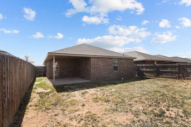 rear view of house featuring roof with shingles, a fenced backyard, a patio area, a lawn, and brick siding