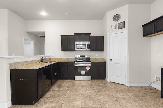 kitchen with baseboards, light stone countertops, a peninsula, appliances with stainless steel finishes, and a sink