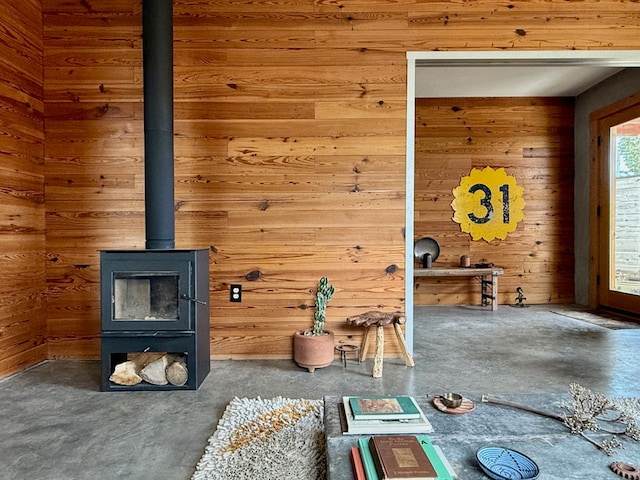 unfurnished living room featuring wood walls, a wood stove, and concrete floors