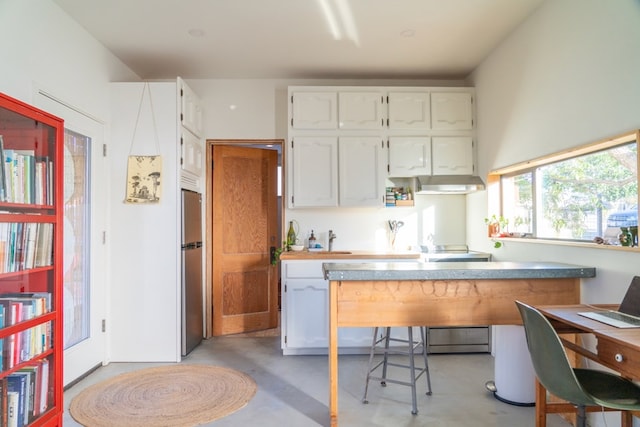 kitchen featuring a breakfast bar, stove, kitchen peninsula, white cabinetry, and stainless steel refrigerator