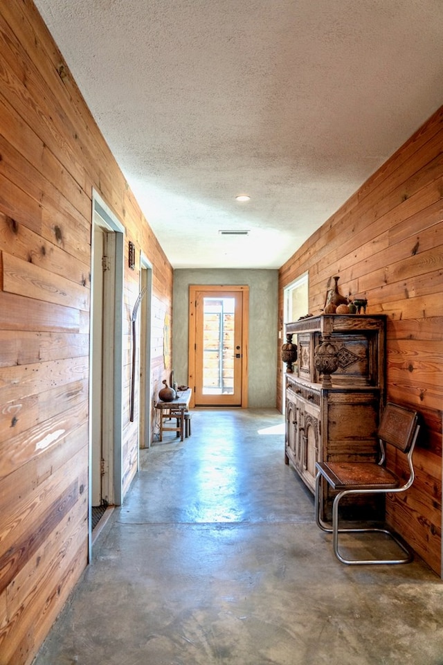 misc room with a textured ceiling, concrete floors, and wood walls