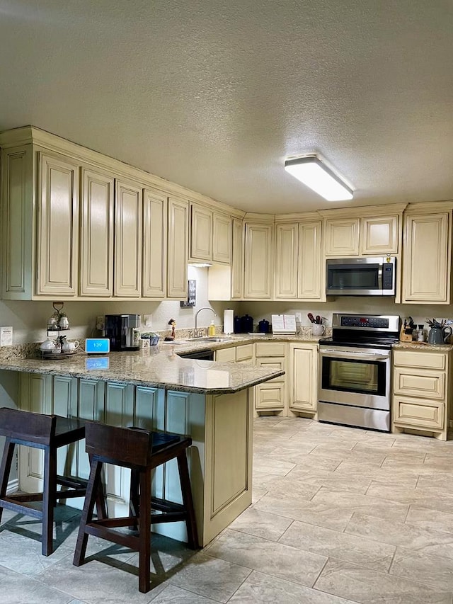 kitchen featuring kitchen peninsula, appliances with stainless steel finishes, a breakfast bar, a textured ceiling, and cream cabinets