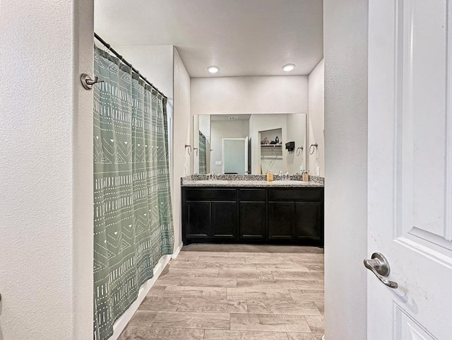 bathroom featuring curtained shower, double vanity, wood finish floors, and a sink