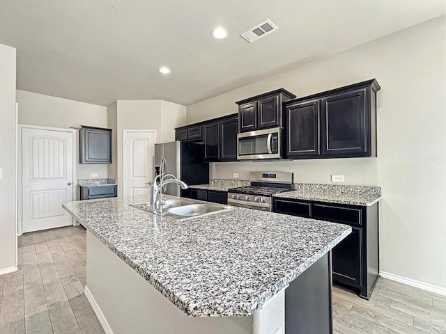 kitchen with wood finish floors, visible vents, a sink, dark cabinetry, and stainless steel appliances