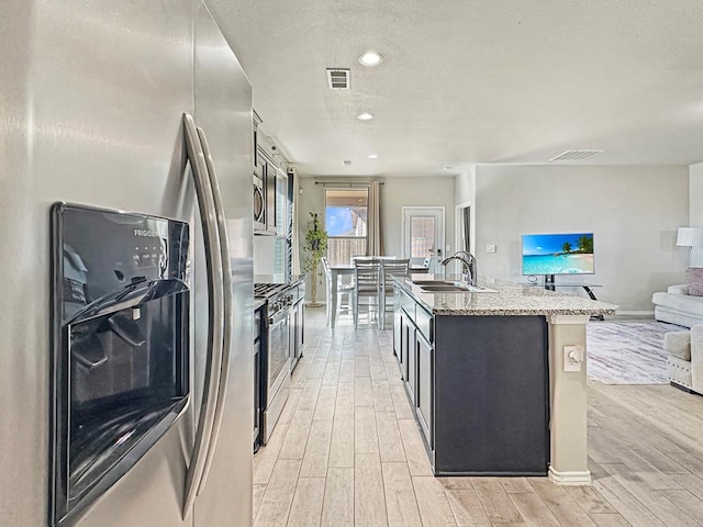 kitchen featuring light wood finished floors, visible vents, open floor plan, stainless steel appliances, and a sink