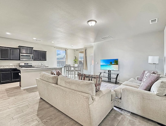 living area with light wood-type flooring, visible vents, baseboards, and a textured ceiling