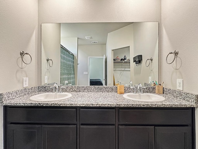 bathroom with a sink, visible vents, double vanity, and a textured wall