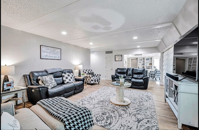 living room with a textured ceiling, light wood-type flooring, and built in shelves