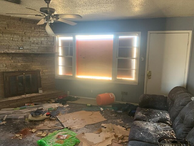 living area with a stone fireplace, ceiling fan, and a textured ceiling