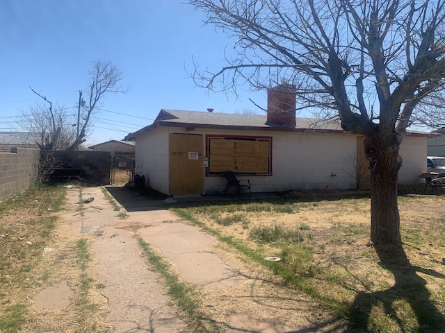 exterior space with concrete block siding, fence, driveway, and a chimney