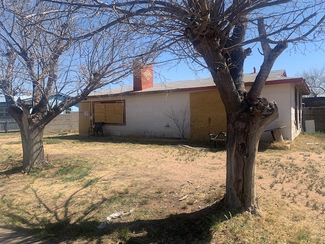 view of side of property with concrete block siding, fence, and a chimney