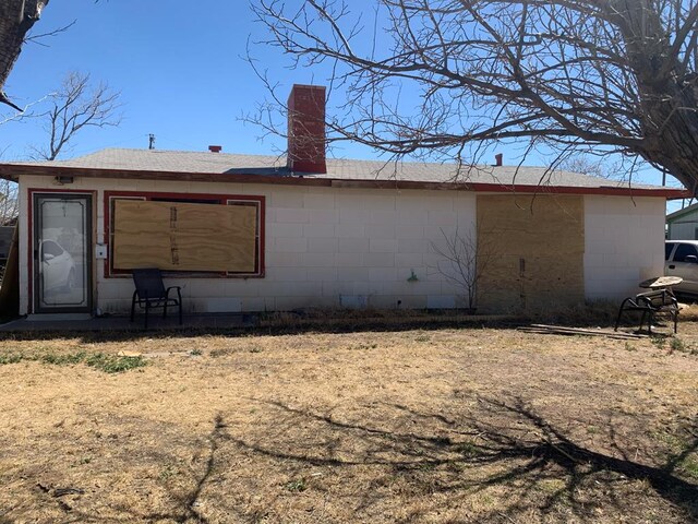 back of house featuring roof with shingles, concrete block siding, and a chimney