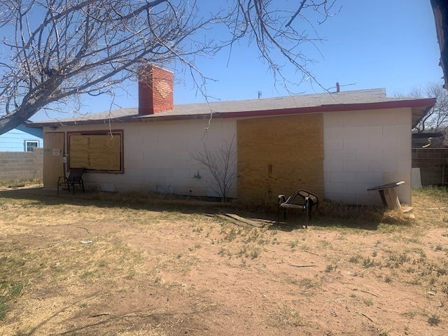 back of property featuring concrete block siding, a chimney, and fence