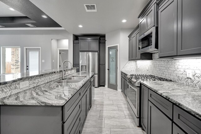 kitchen with tasteful backsplash, visible vents, light stone countertops, stainless steel appliances, and a sink