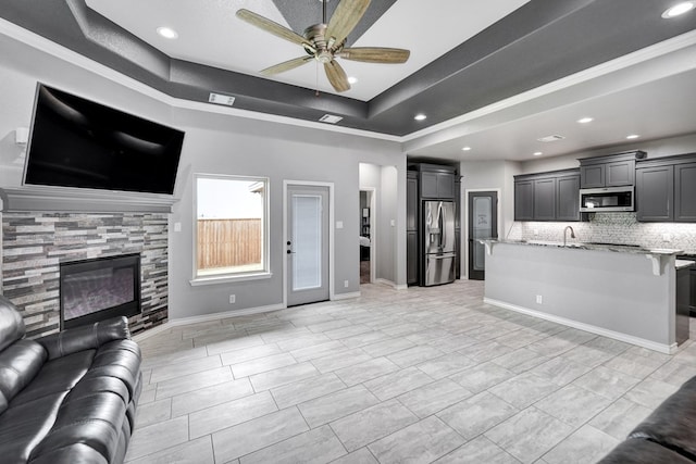 living area featuring visible vents, baseboards, ceiling fan, a glass covered fireplace, and a raised ceiling