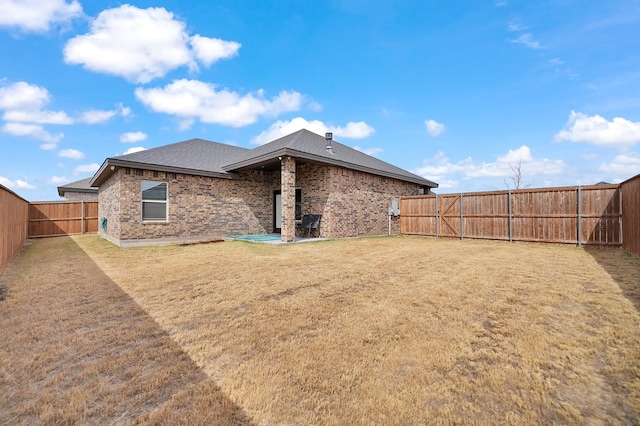 rear view of house featuring a patio, roof with shingles, a fenced backyard, a lawn, and brick siding