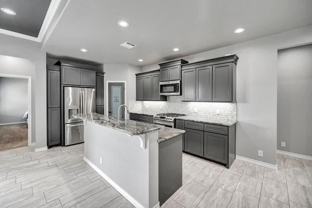 kitchen featuring tasteful backsplash, visible vents, light stone counters, stainless steel appliances, and a kitchen island with sink