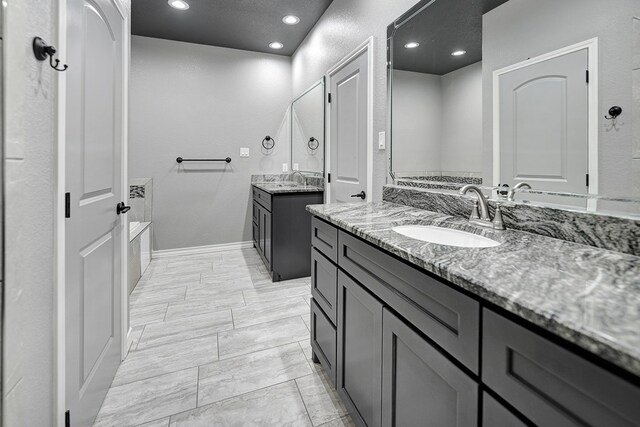 bathroom featuring baseboards, two vanities, recessed lighting, a sink, and a bathtub