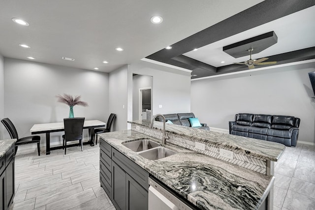 kitchen featuring ceiling fan, light stone countertops, open floor plan, and a sink