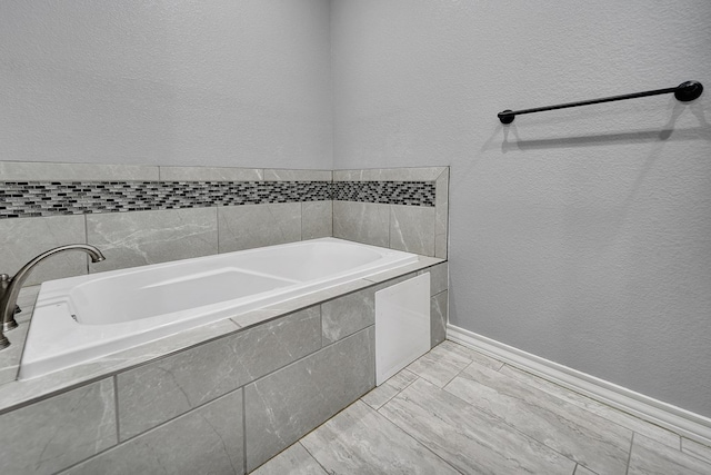 full bathroom featuring baseboards, a garden tub, and a textured wall