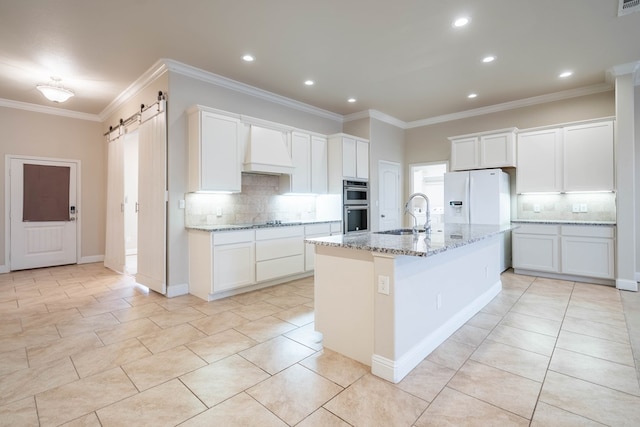 kitchen with an island with sink, custom range hood, white fridge with ice dispenser, a barn door, and white cabinets