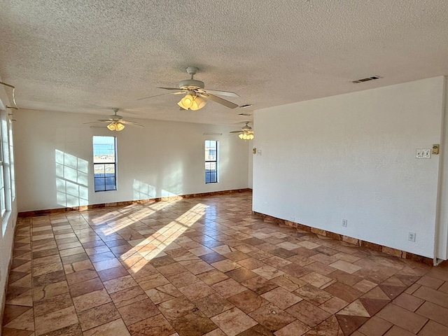 empty room featuring a wealth of natural light, ceiling fan, and a textured ceiling