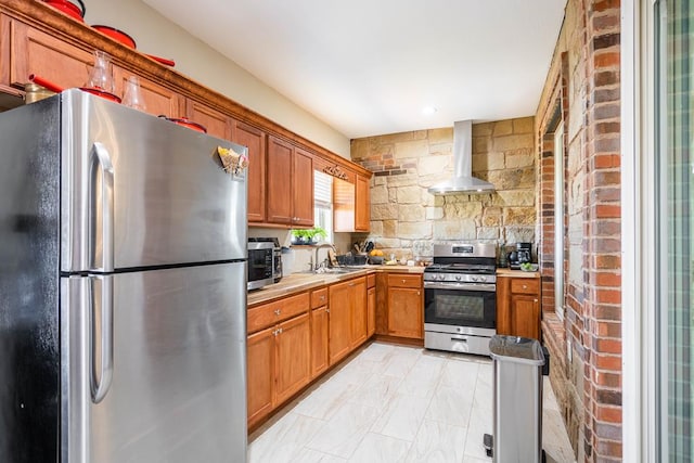 kitchen with appliances with stainless steel finishes, sink, and wall chimney range hood