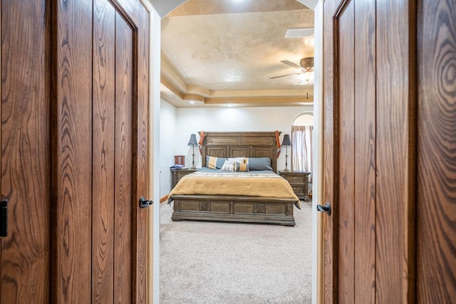 carpeted bedroom with a tray ceiling and ceiling fan