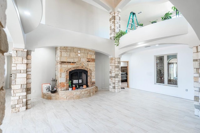 living room featuring a stone fireplace, a towering ceiling, and decorative columns