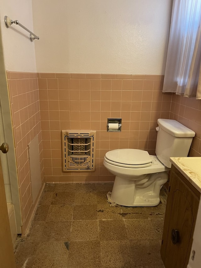 bathroom featuring tile walls, toilet, heating unit, and vanity