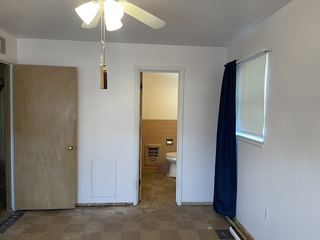 unfurnished bedroom with ceiling fan, tile walls, heating unit, and connected bathroom