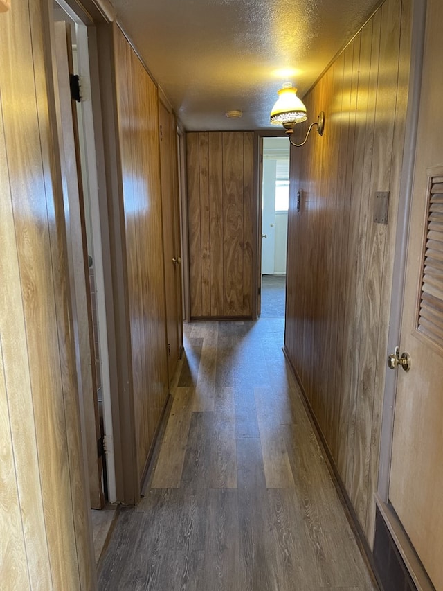 corridor featuring wood-type flooring, wood walls, and a textured ceiling