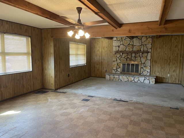 unfurnished living room featuring a textured ceiling, a stone fireplace, beam ceiling, and wooden walls