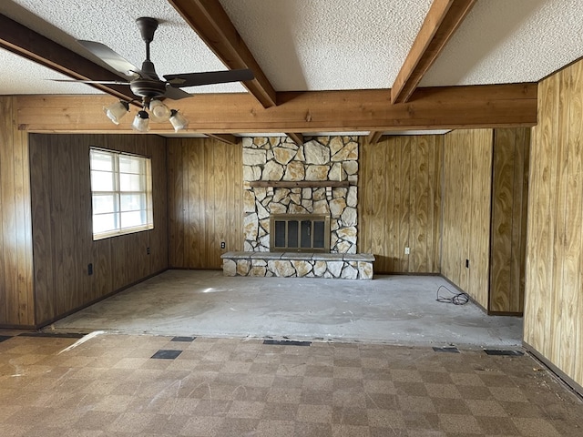 unfurnished living room featuring a stone fireplace, a textured ceiling, wood walls, and beamed ceiling