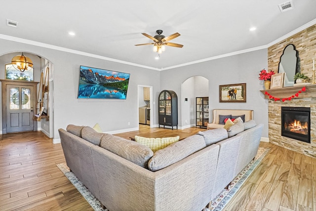 living room featuring crown molding, a stone fireplace, ceiling fan, and light hardwood / wood-style flooring