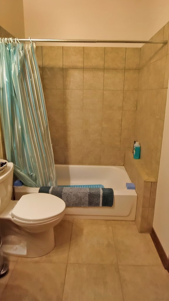 bathroom with tile patterned flooring, shower / bathtub combination with curtain, and toilet