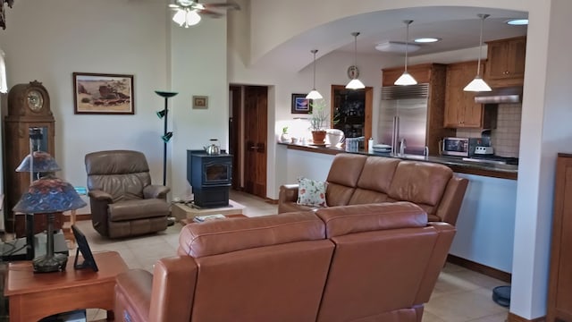 living room with ceiling fan, a wood stove, and light tile patterned floors