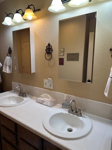 full bath with a textured wall, double vanity, and a sink