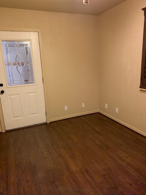 unfurnished room featuring baseboards and dark wood-type flooring