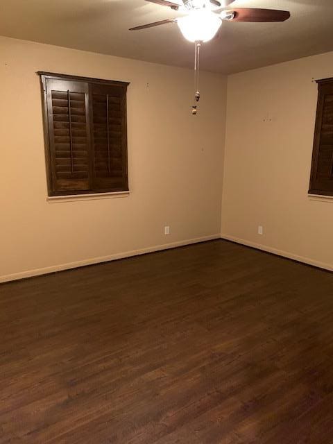 empty room with dark wood finished floors, a ceiling fan, and baseboards