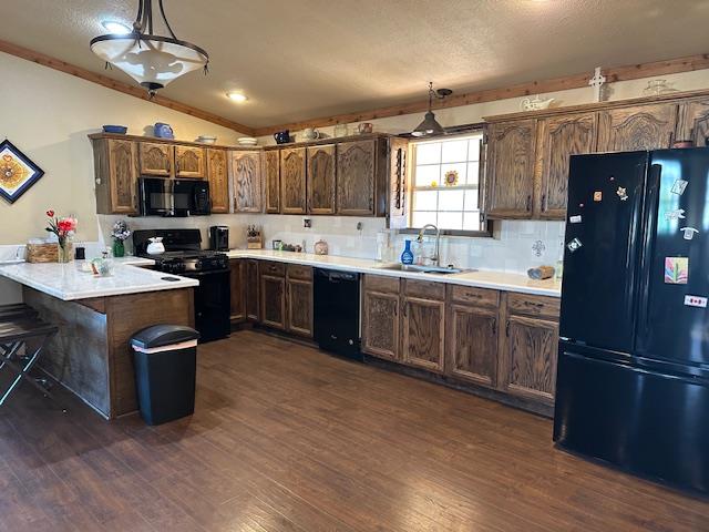 kitchen with hanging light fixtures, a peninsula, light countertops, black appliances, and a sink