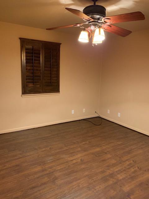 unfurnished room with dark wood-style floors, baseboards, and a ceiling fan