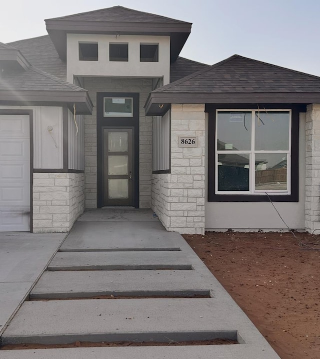 view of exterior entry with a garage, stone siding, and a shingled roof