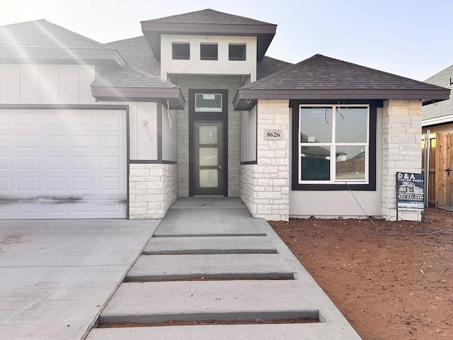 property entrance with a garage, stone siding, roof with shingles, and fence