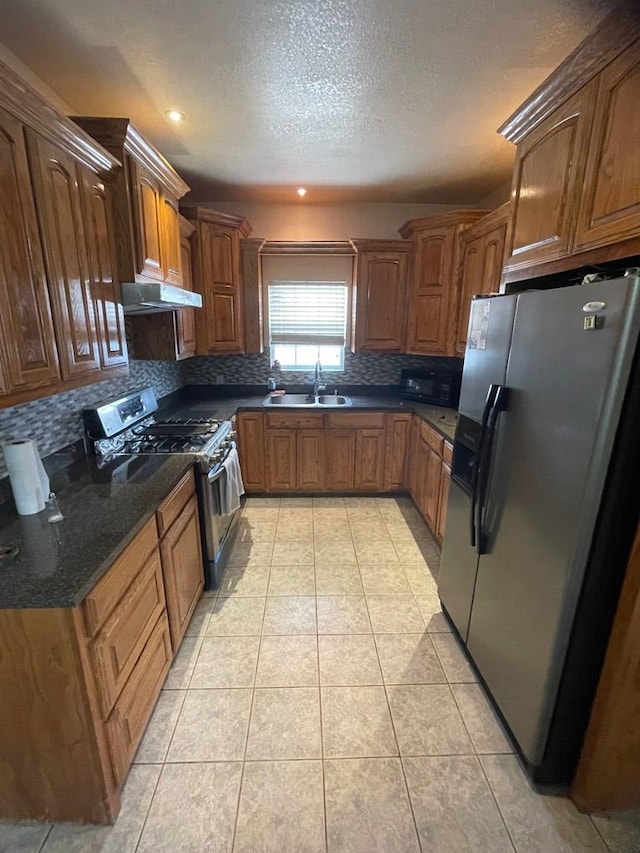 kitchen with dark stone countertops, sink, tasteful backsplash, light tile patterned floors, and appliances with stainless steel finishes