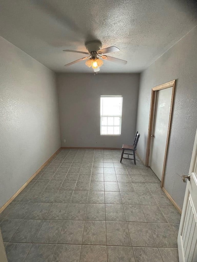 tiled empty room with ceiling fan and a textured ceiling