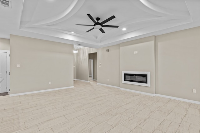 unfurnished living room with ceiling fan and a tray ceiling