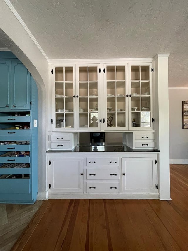 bar featuring white cabinets, a textured ceiling, crown molding, and dark wood-type flooring