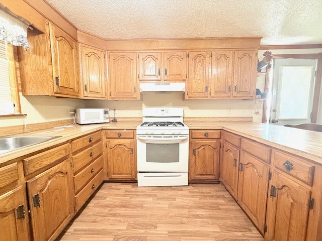 kitchen featuring light wood finished floors, under cabinet range hood, light countertops, white appliances, and a textured ceiling